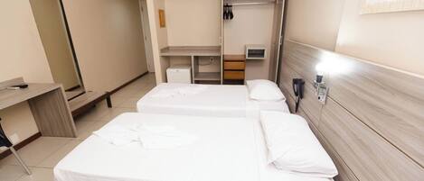 Een hotelkamer met drie eenpersoonsbedden, een bureau, een spiegel en een kledingkast.