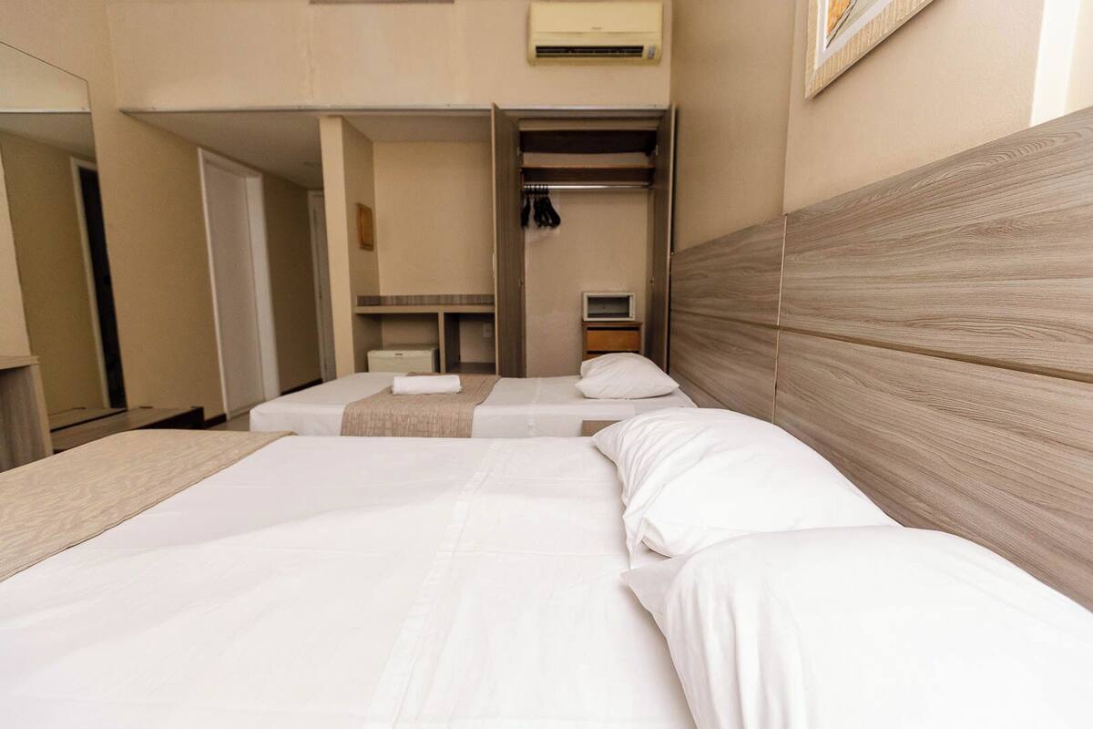 A hotel room with two beds, a wooden headboard, a wardrobe, and a small desk with a chair.