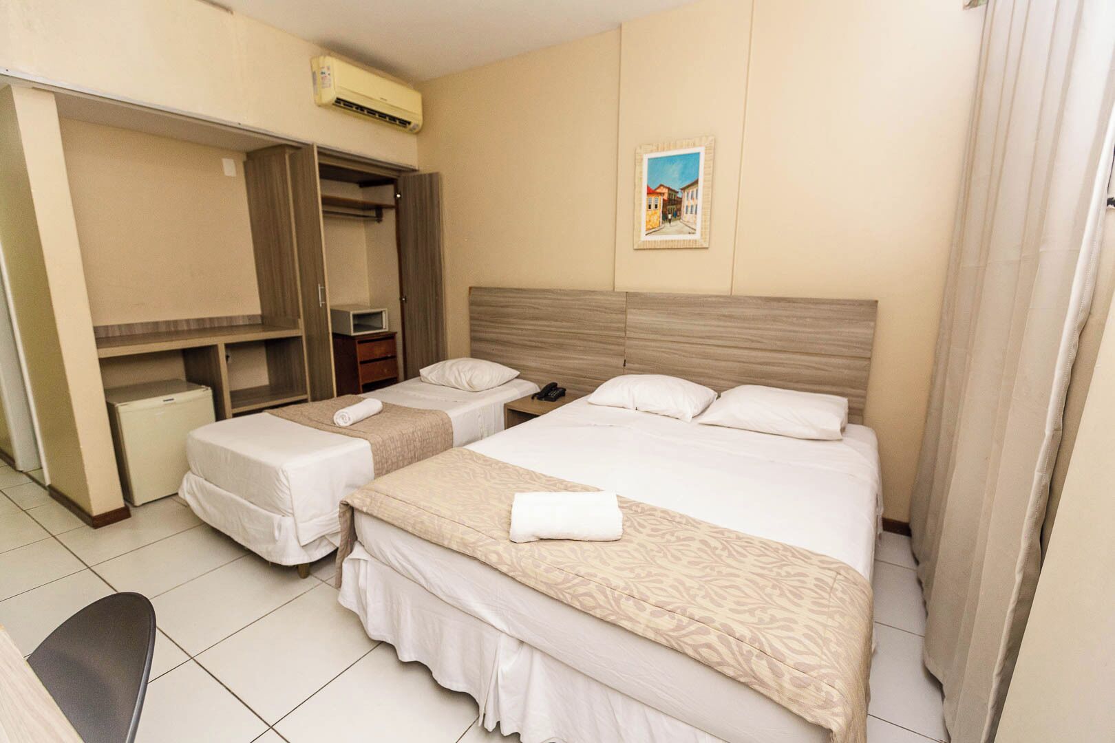 Une chambre d’hôtel avec deux lits, une armoire, un bureau et un appareil de climatisation.