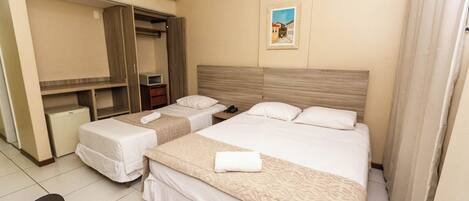 A hotel room with two beds, a wardrobe, a desk, and an air conditioning unit.