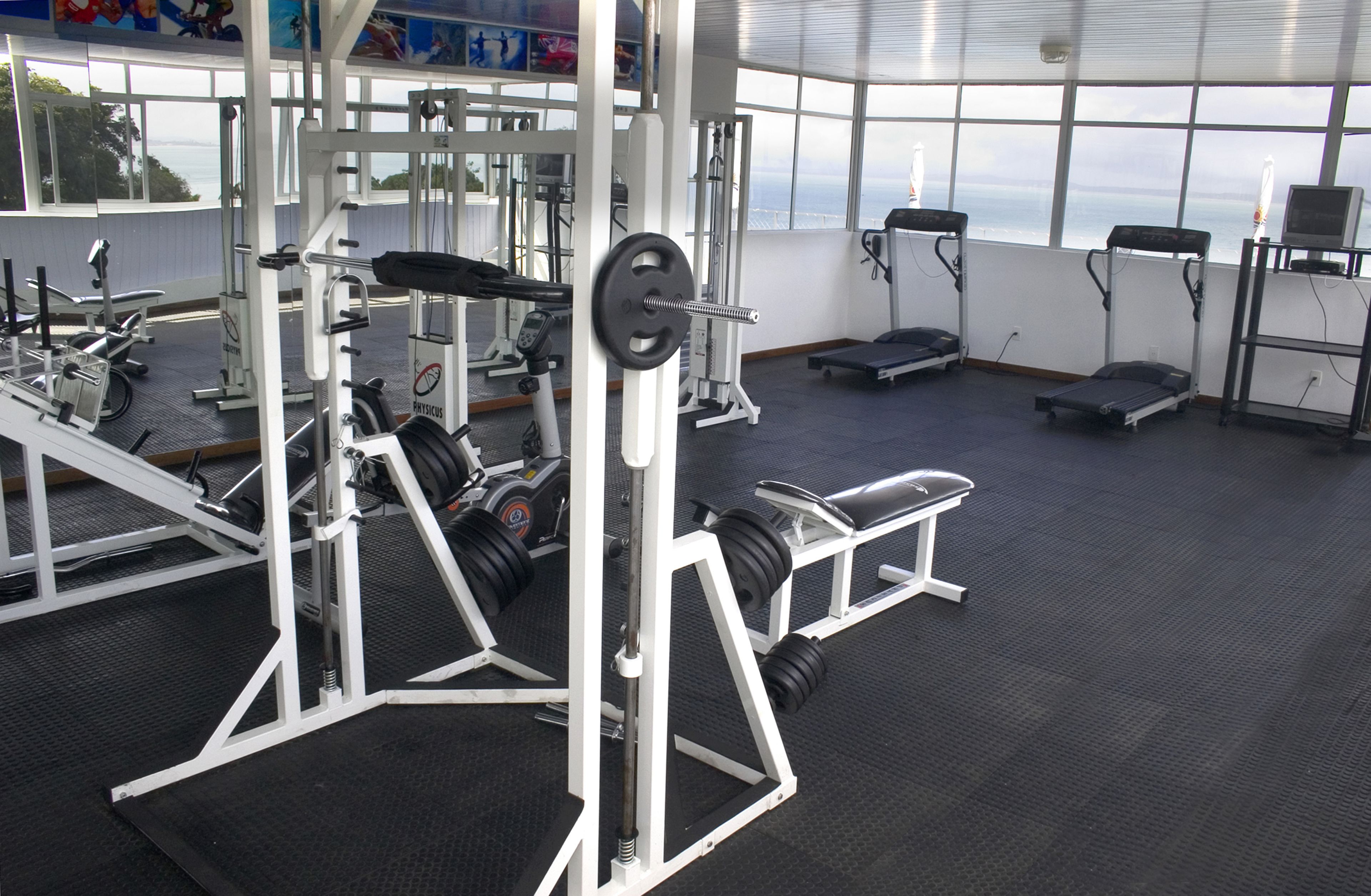 A gym with various exercise equipment, including weight machines and benches, with large windows offering a view of the ocean.