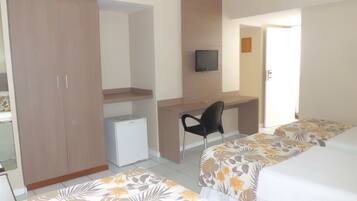 Quarto de hotel com cama, escrivaninha, cadeira, televisão e guarda-roupa.
