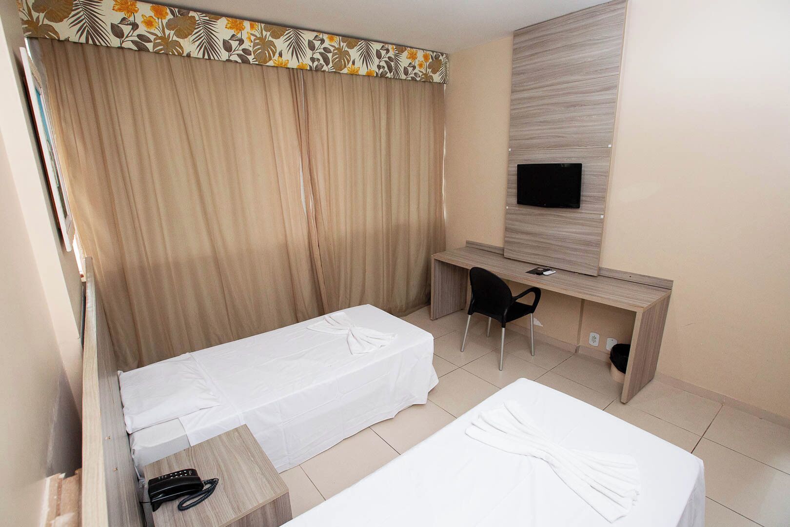 Una habitación de hotel con dos camas, un escritorio, una silla, un televisor y una cortina estampada con motivos florales.