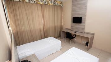 Una habitación de hotel con dos camas, un escritorio, una silla, un televisor y una cortina estampada con motivos florales.