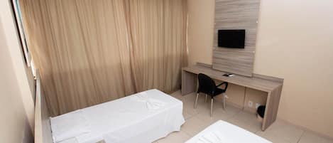 Una habitación de hotel con dos camas, un escritorio, una silla, un televisor y una cortina estampada con motivos florales.