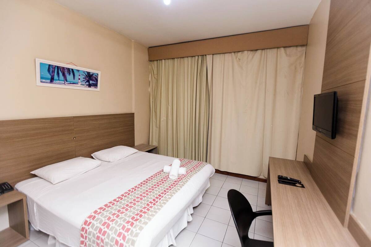 A hotel room with a bed, a desk, a chair, a television, and a window with curtains.