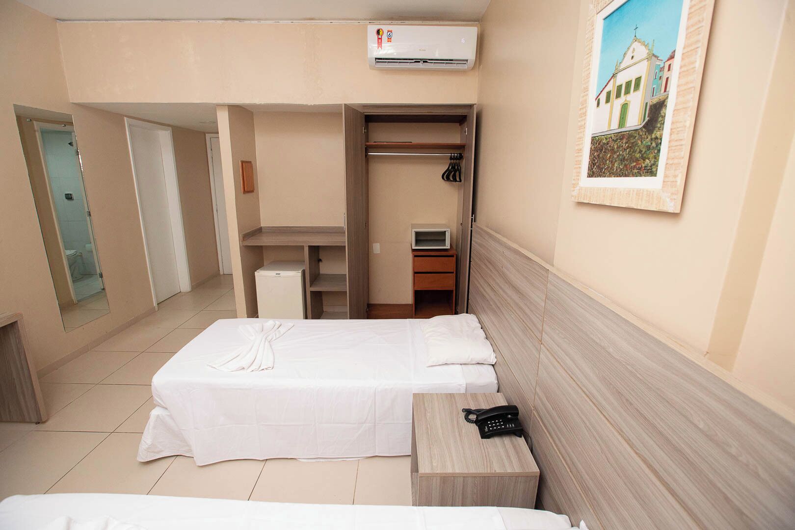 Une chambre d’hôtel comprenant un lit, une table de chevet avec un téléphone, une armoire et un petit bureau avec une télévision.