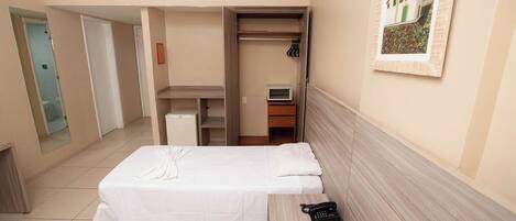 Une chambre d’hôtel comprenant un lit, une table de chevet avec un téléphone, une armoire et un petit bureau avec une télévision.