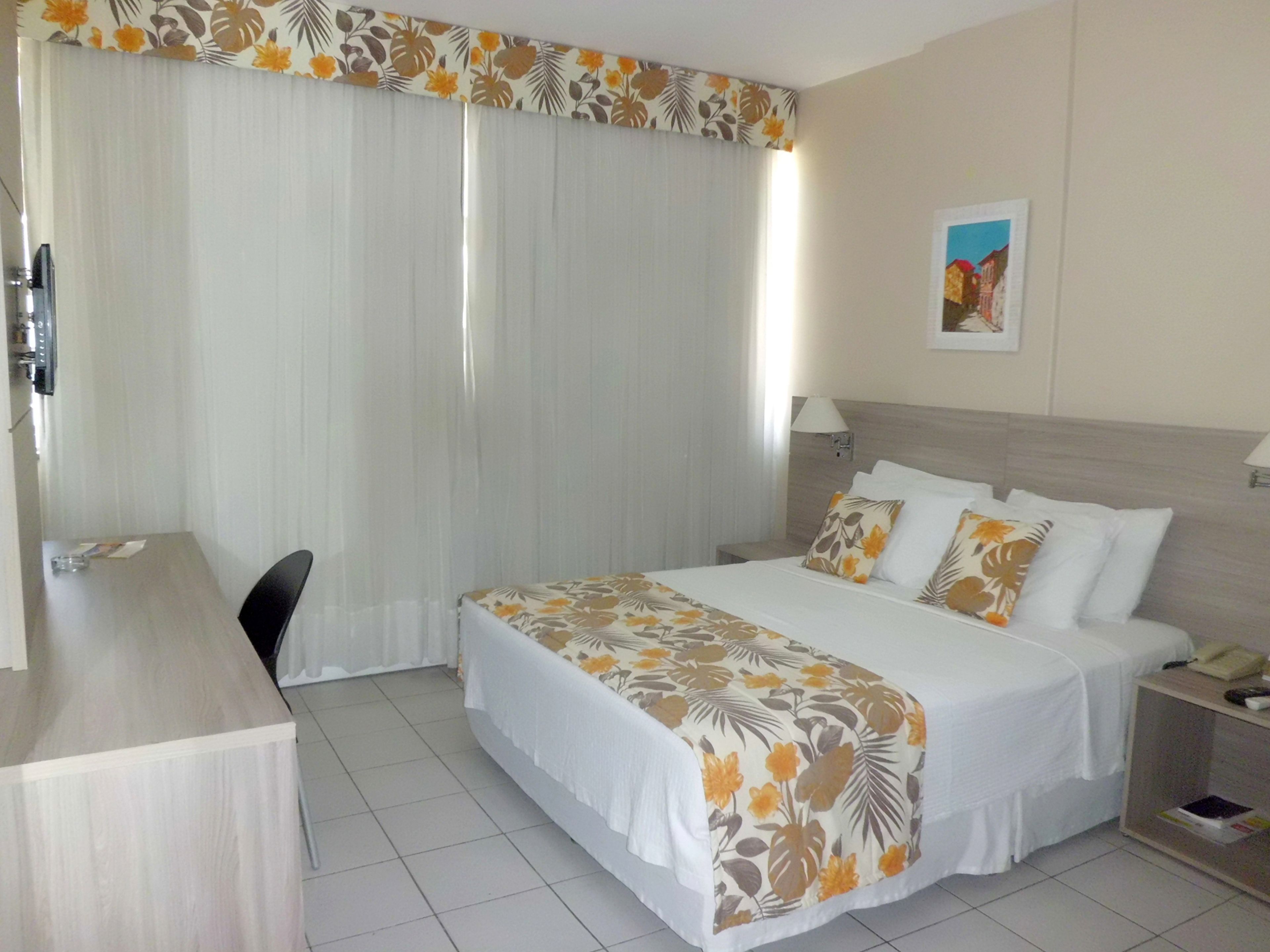 A hotel room with a bed, a desk, a nightstand, and a wall-mounted lamp.