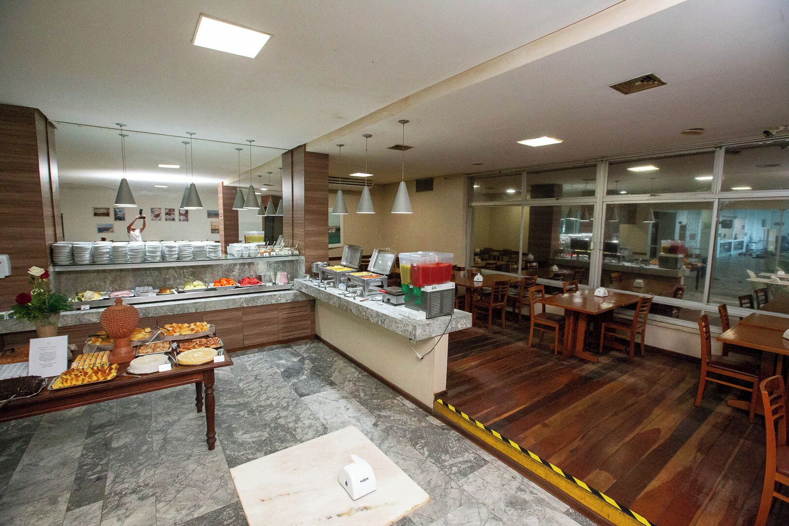 Un restaurante moderno con zona de bufé, suelo de mármol y mesas y sillas de madera.