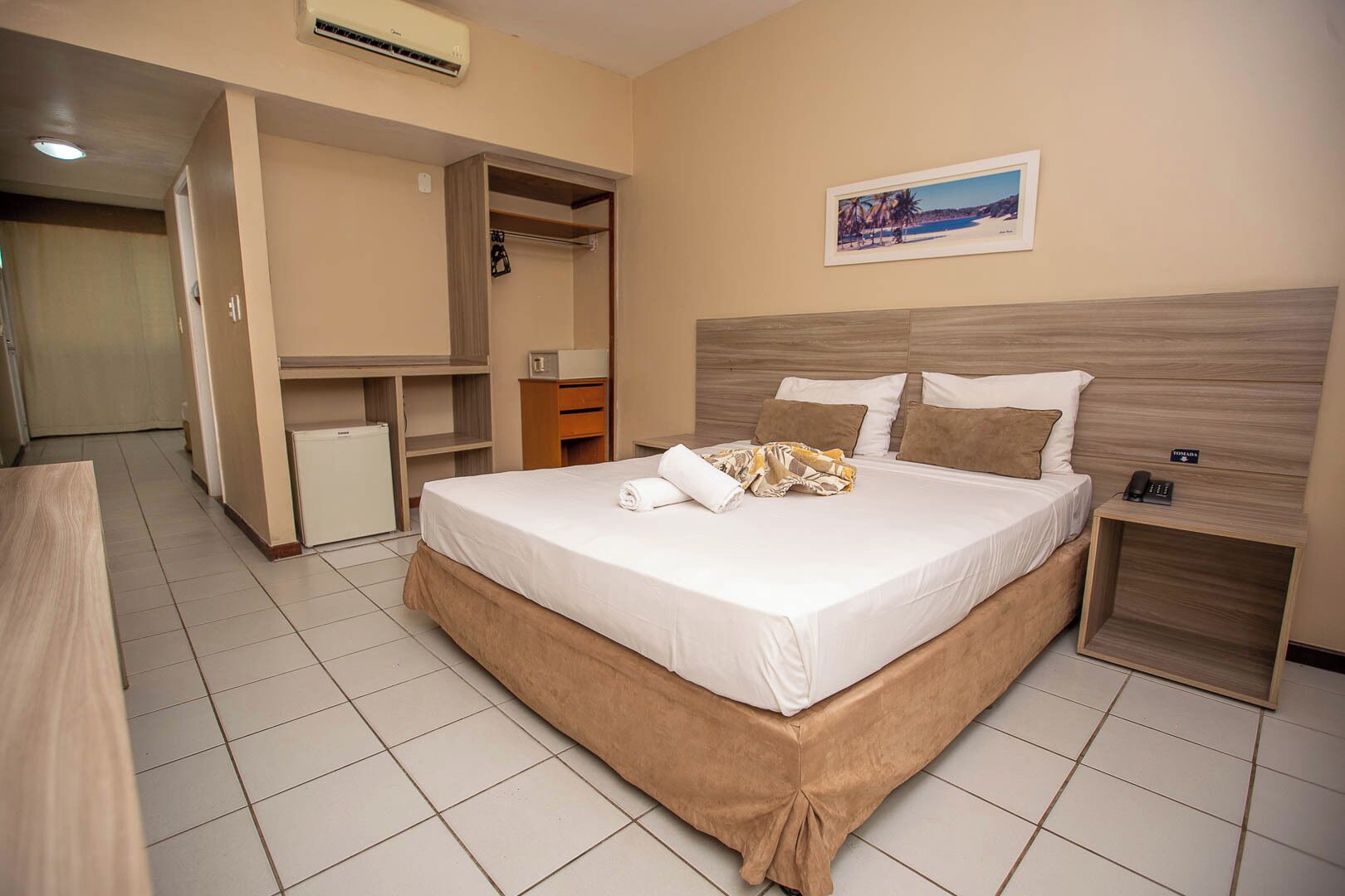 A hotel room with a bed, a desk, a wardrobe, and a small refrigerator.