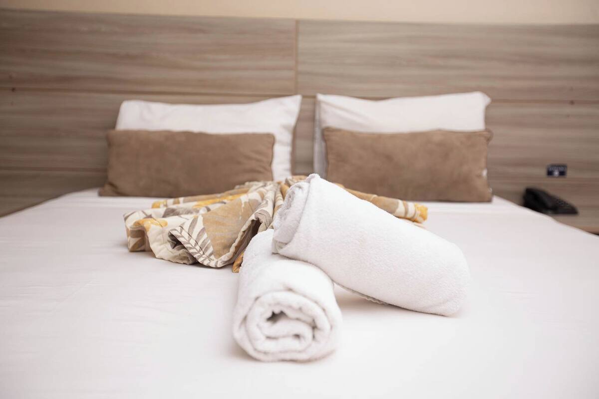A neatly made bed with two pillows, a rolled white towel, and a folded blanket.
