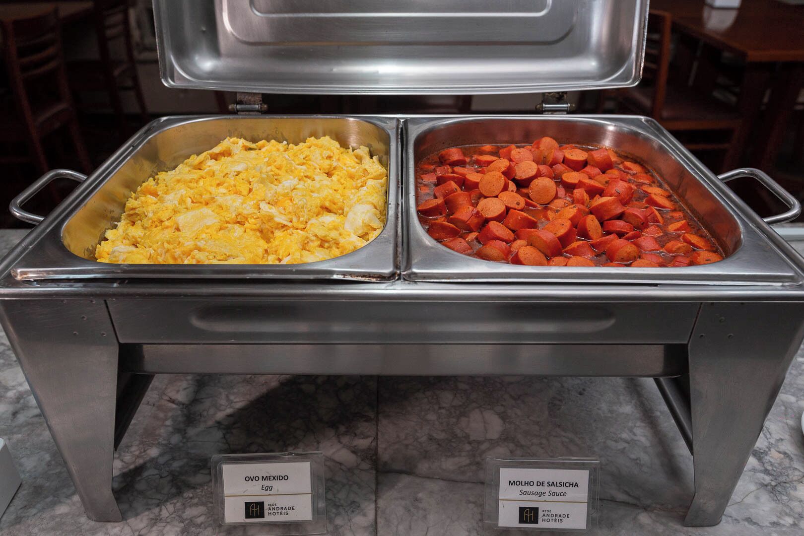 A buffet with scrambled eggs and sausage slices.