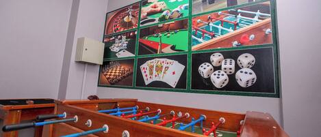 A room with a foosball table and a wall decorated with various board games and dice.