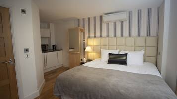 A hotel room with a bed, a bedside table, a lamp, a wardrobe, a mirror, and a kitchenette.
