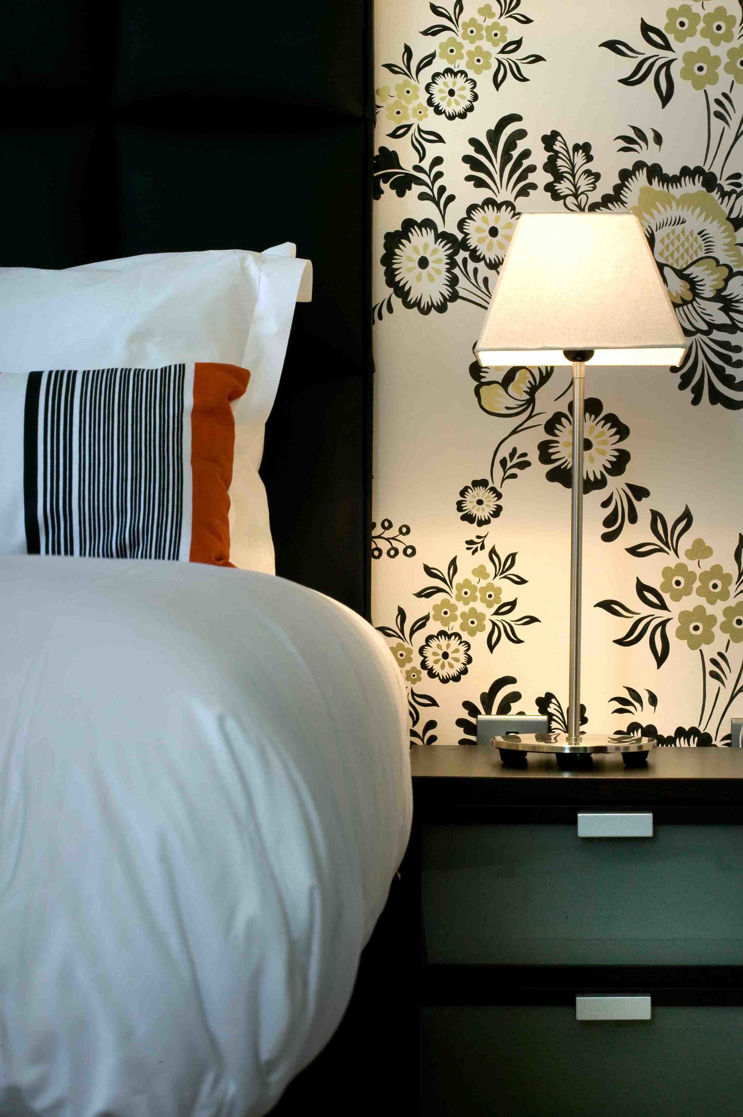 A neatly made bed with white and orange bedding, a striped pillow, and a bedside table with a lamp.