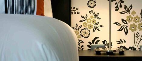 A neatly made bed with white and orange bedding, a striped pillow, and a bedside table with a lamp.