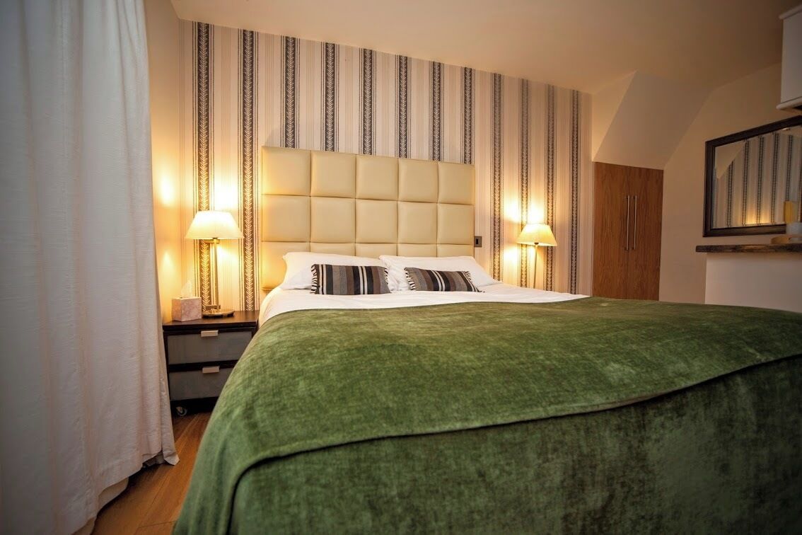 A neatly made bed with a green cover, two bedside lamps, and a striped wall pattern.