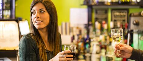 Una persona sosteniendo una copa de vino en un bar, con estantes llenos de botellas al fondo.