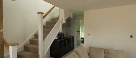 A modern living room with a beige sofa, a staircase with wooden handrails, and a black entertainment unit.
