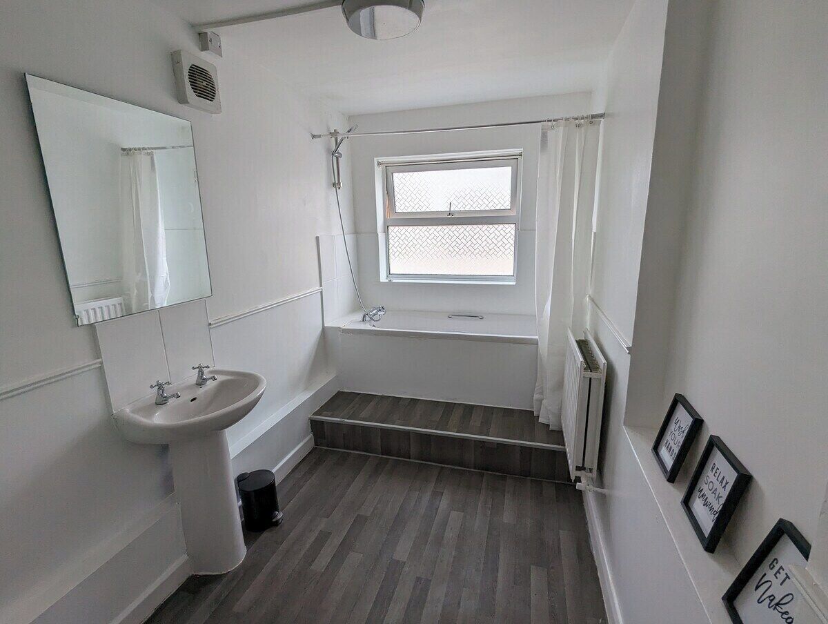 A small bathroom with a sink, a window, and a shower.