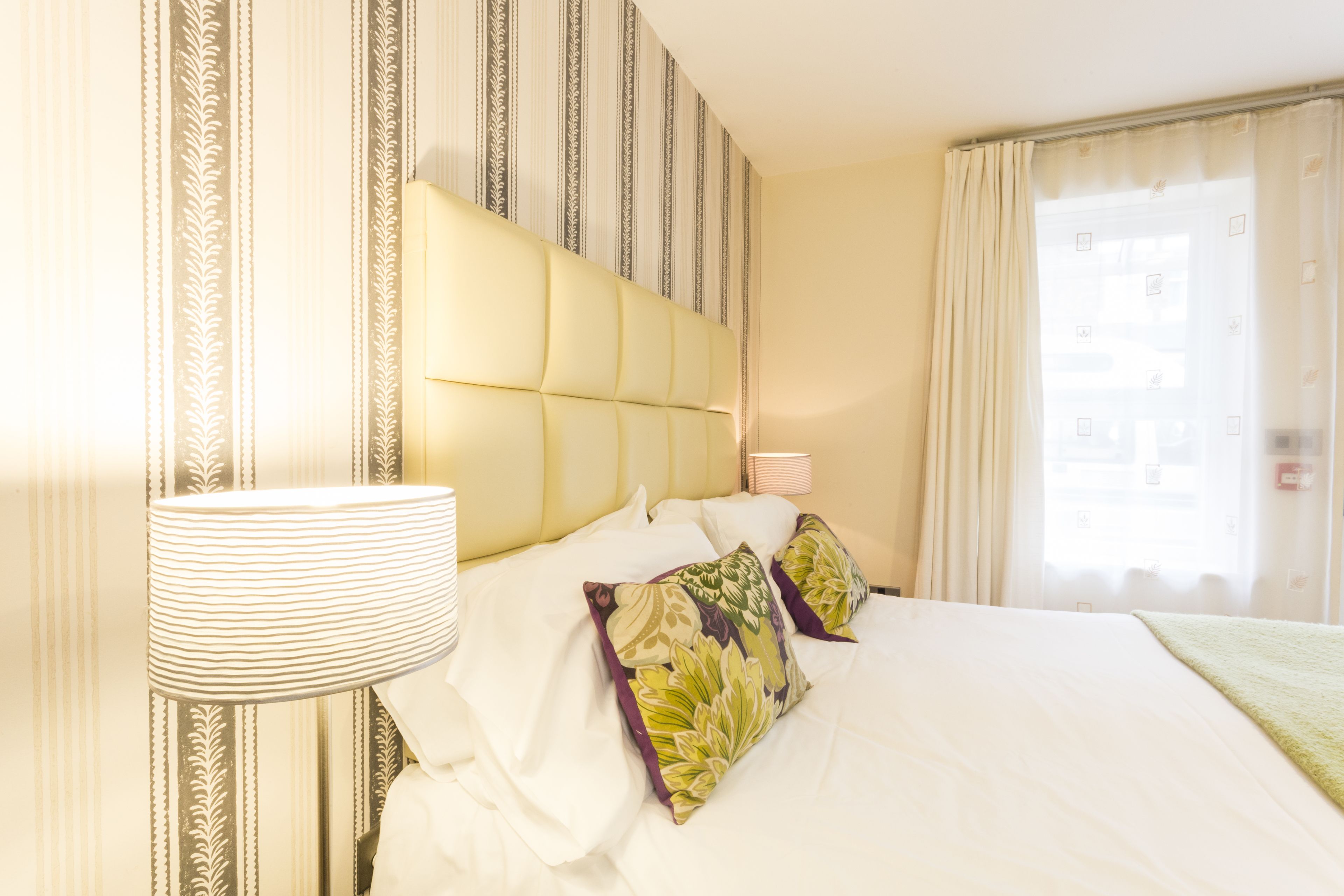 A hotel room with a large bed, striped wallpaper, and a window with curtains.