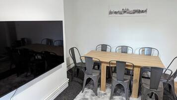 A dining area with a wooden table and six chairs, a cityscape artwork on the wall, and a window with a view of the interior.