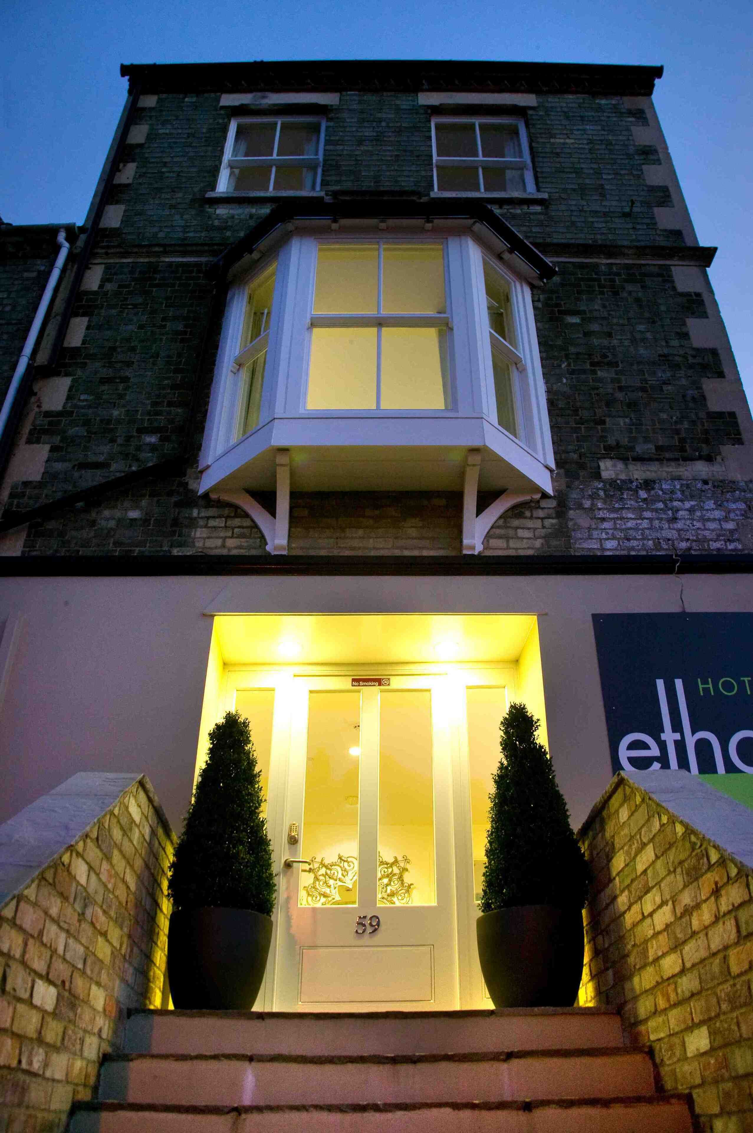 A building with a bay window, a door labeled "59", and two potted plants on the steps.