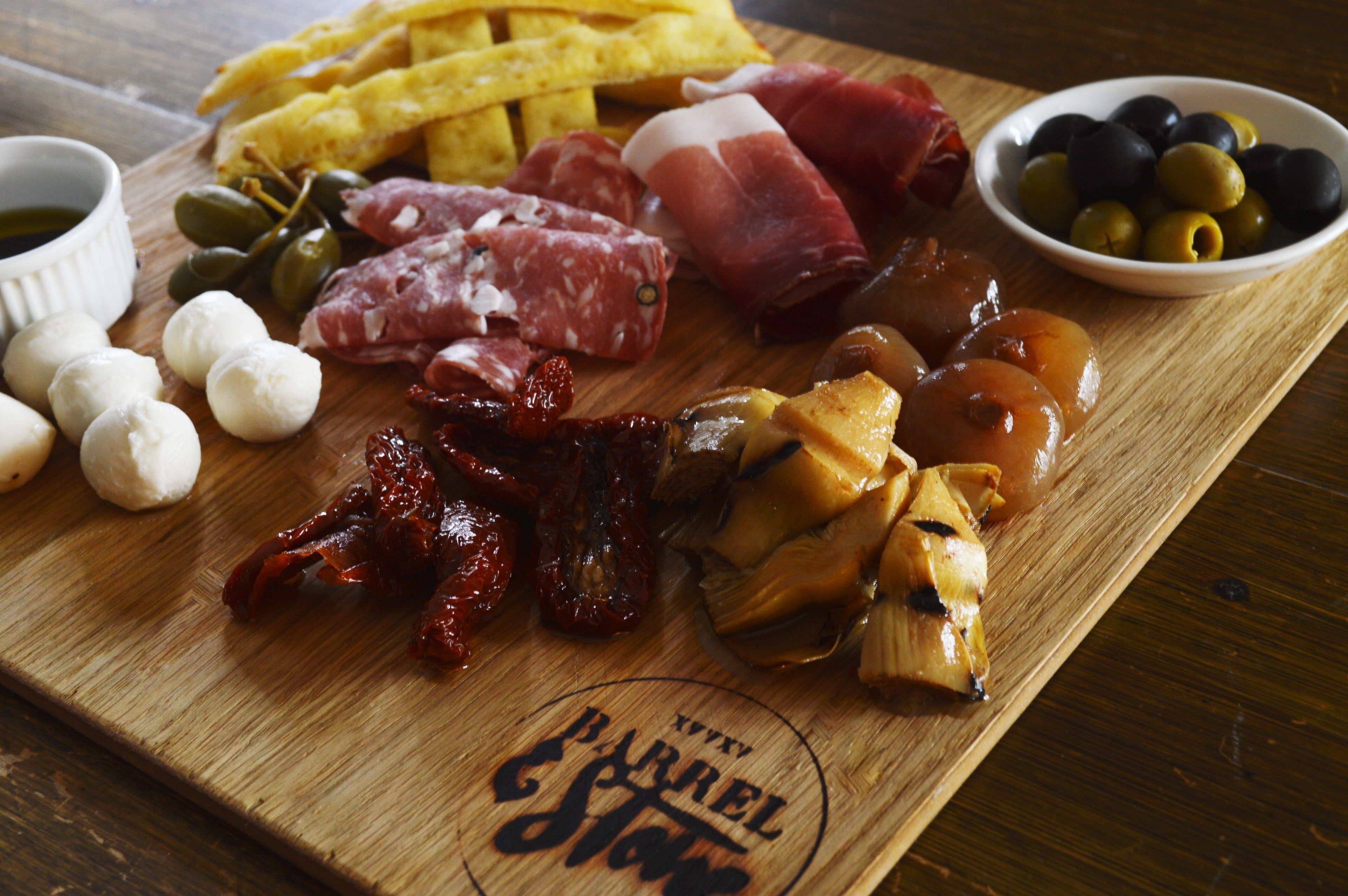 A wooden board with various food items including meats, olives, and cheese.