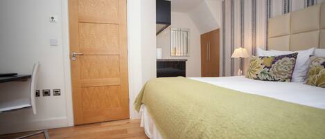 Una habitación de hotel con una puerta de madera, una cama con una manta verde, una lámpara de noche y una pared a rayas.