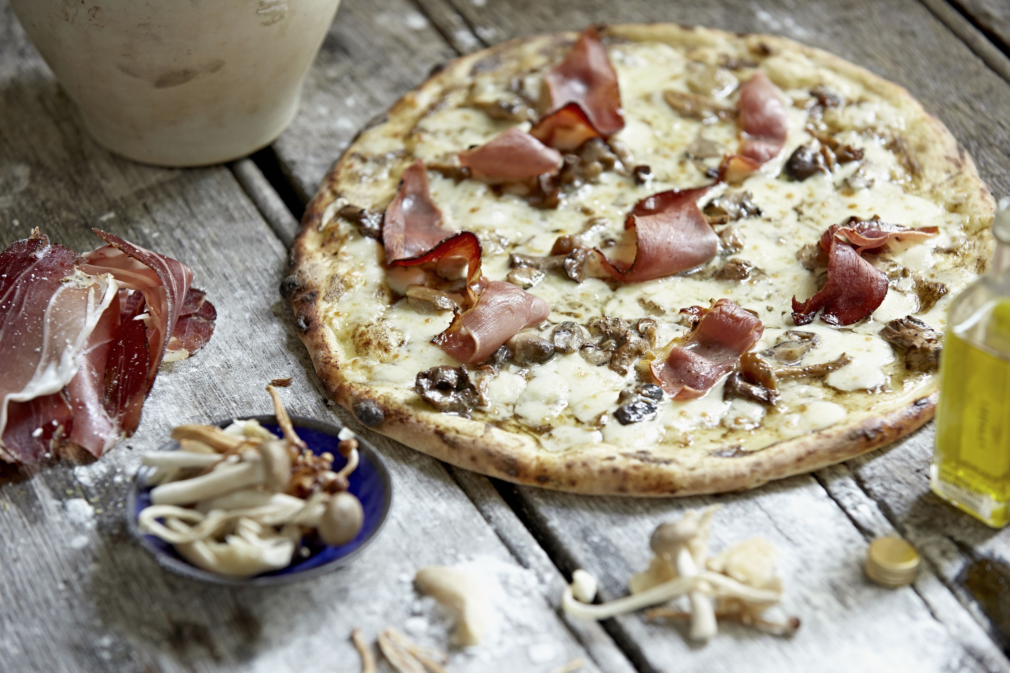Pizza mit Speck und Pilzen auf einem Holztisch.