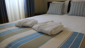 A neatly made bed with striped bedding, a folded towel, and a bedside table with a lamp. - Hotel Ordem de Santiago (Alcacer do Sal)