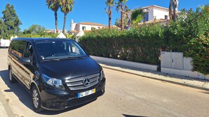 A black Mercedes-Benz SUV parked on a street with a clear blue sky, palm trees, and a white building with a tiled roof in the background. - Hotel Ordem de Santiago (Alcacer do Sal)