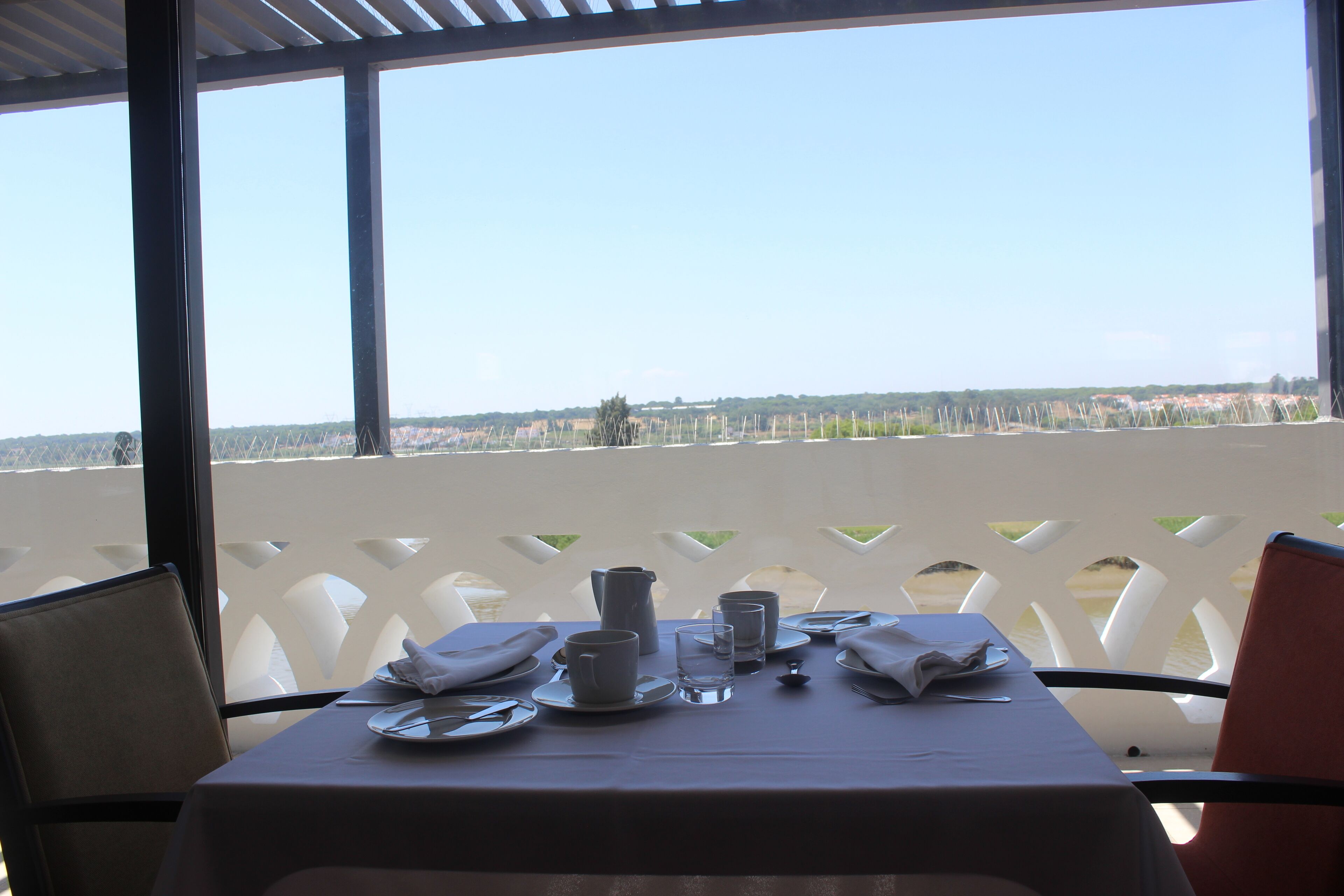 A table set for two with a view of a distant landscape through a white lattice structure.