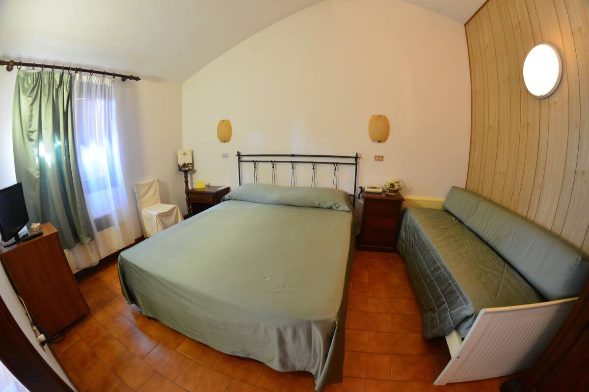 A bedroom with a bed, bedside tables, a chair, a TV, and a sofa.