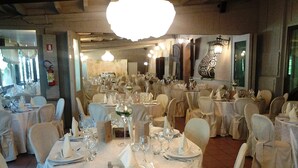 A banquet hall with round tables set for a formal event, featuring white tablecloths, chairs with white covers, and a chandelier. - Panazza Hotel (Mordano)