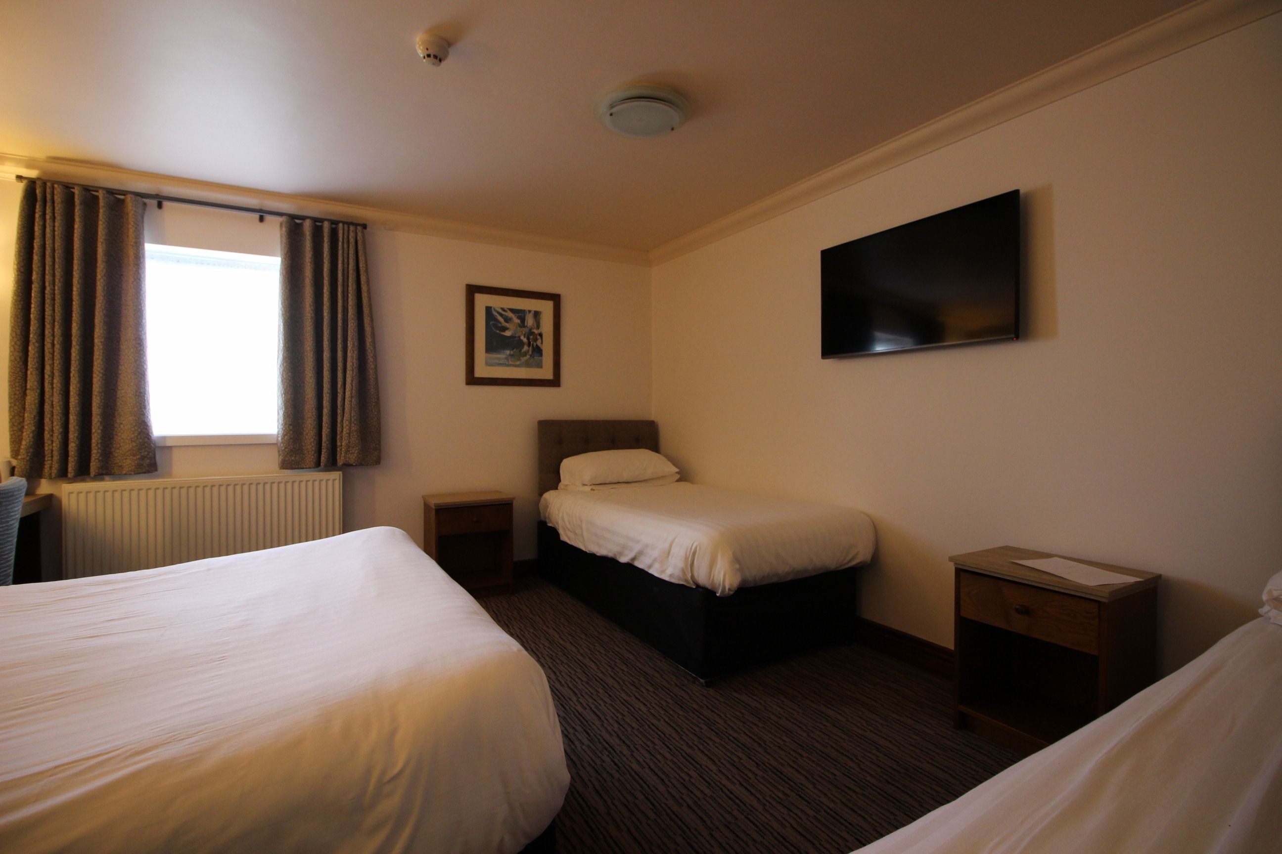 A hotel room with two beds, a flat-screen TV, a framed picture on the wall, and a window with curtains.
