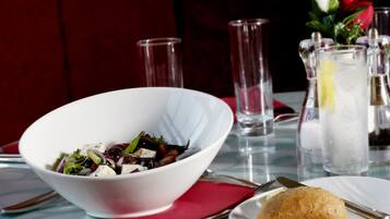 Une table à manger avec un saladier blanc rempli de salade, une assiette avec une pâtisserie et un verre d’eau.