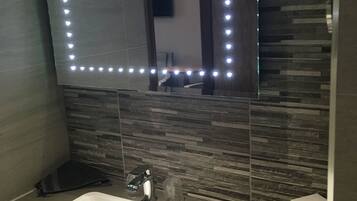 A bathroom with a white sink, a mirror with LED lights, and a tiled wall.
