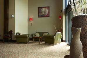 A room with a patterned carpet, a green sofa set, a wooden coffee table, and a large vase. - Pastures Hotel (Doncaster)