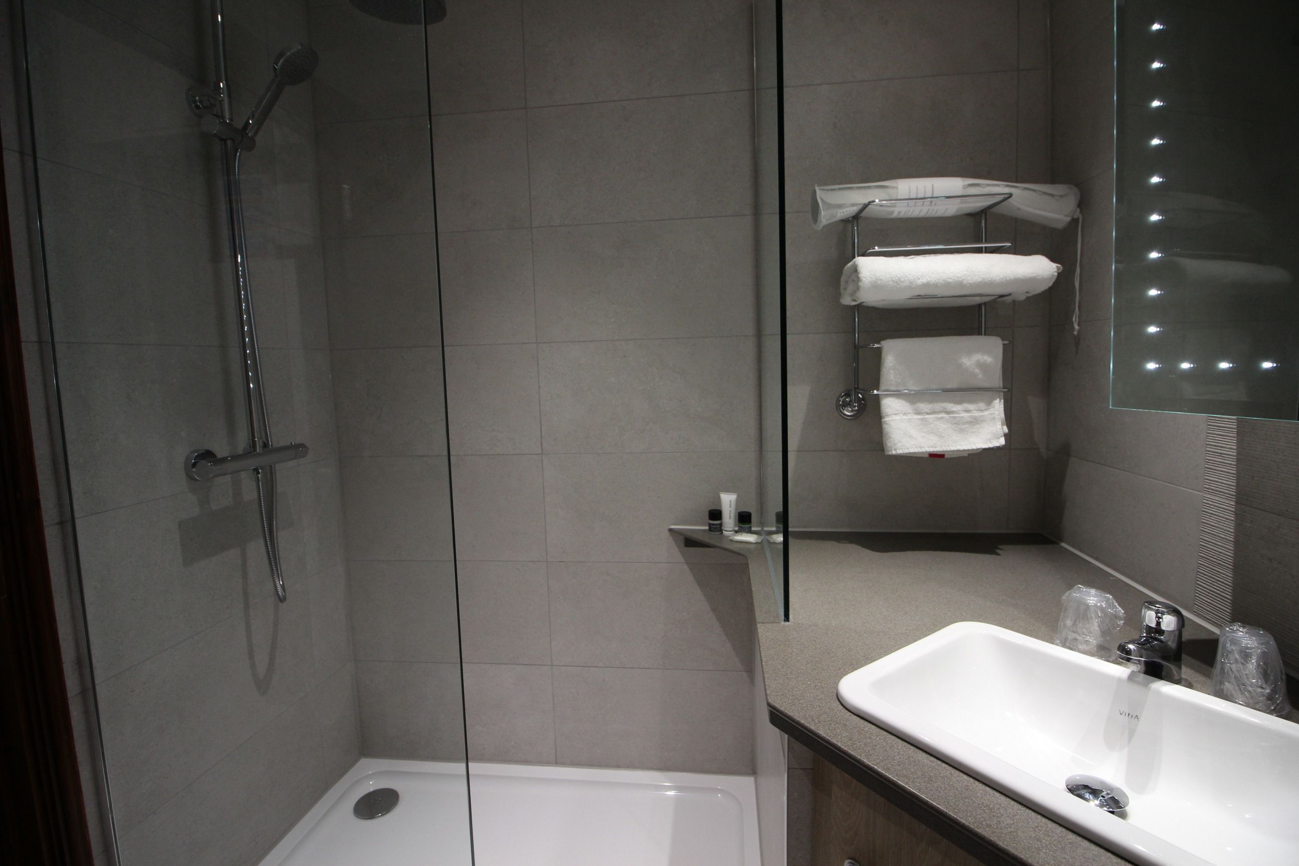 Un baño moderno con ducha de vidrio, lavabo blanco y espejo con luces.