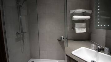 Un baño moderno con ducha de vidrio, lavabo blanco y espejo con luces.
