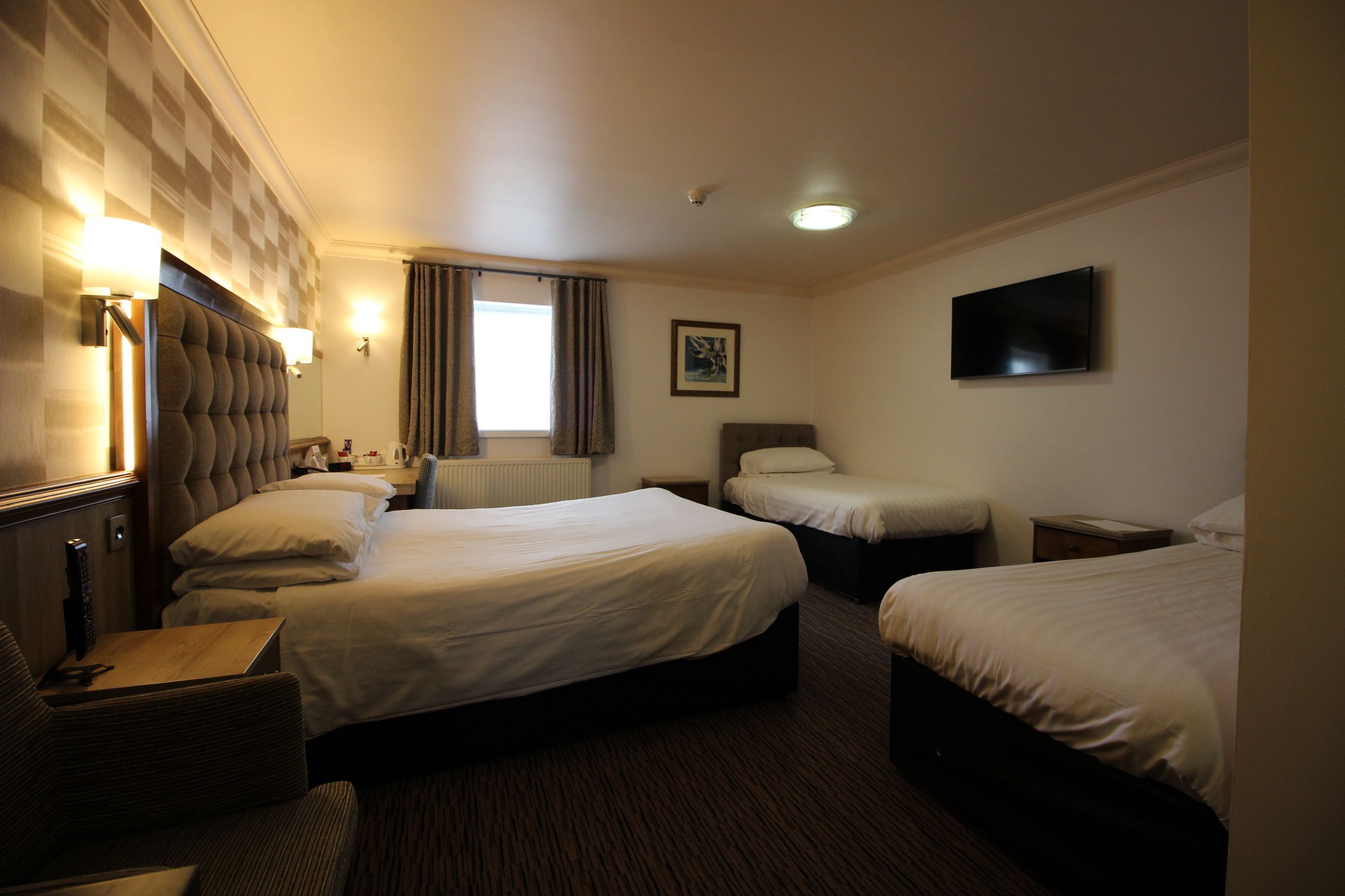 A hotel room with two beds, a sofa, a television, and a window with curtains.