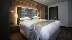 A modern hotel room with a large bed, a wooden headboard, and a built-in nightstand. - Pastures Hotel (Doncaster)