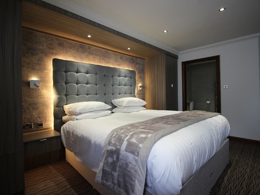 A modern hotel room with a large bed, a wooden headboard, and a built-in nightstand.