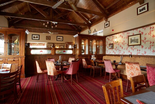 A restaurant with wooden furniture, a red striped carpet, and a brick wall. - Pastures Hotel (Doncaster)