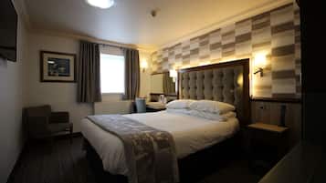 Een hotelkamer met een groot bed, een bureau, een stoel, een raam met gordijnen, een wandtelevisie en een lamp.