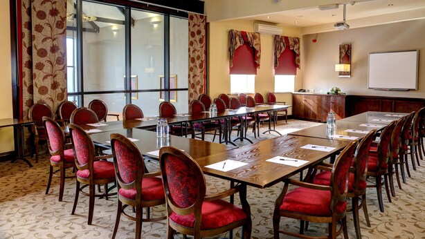 A conference room with a long table, red upholstered chairs, a projector screen, and a whiteboard. - Pastures Hotel (Doncaster)