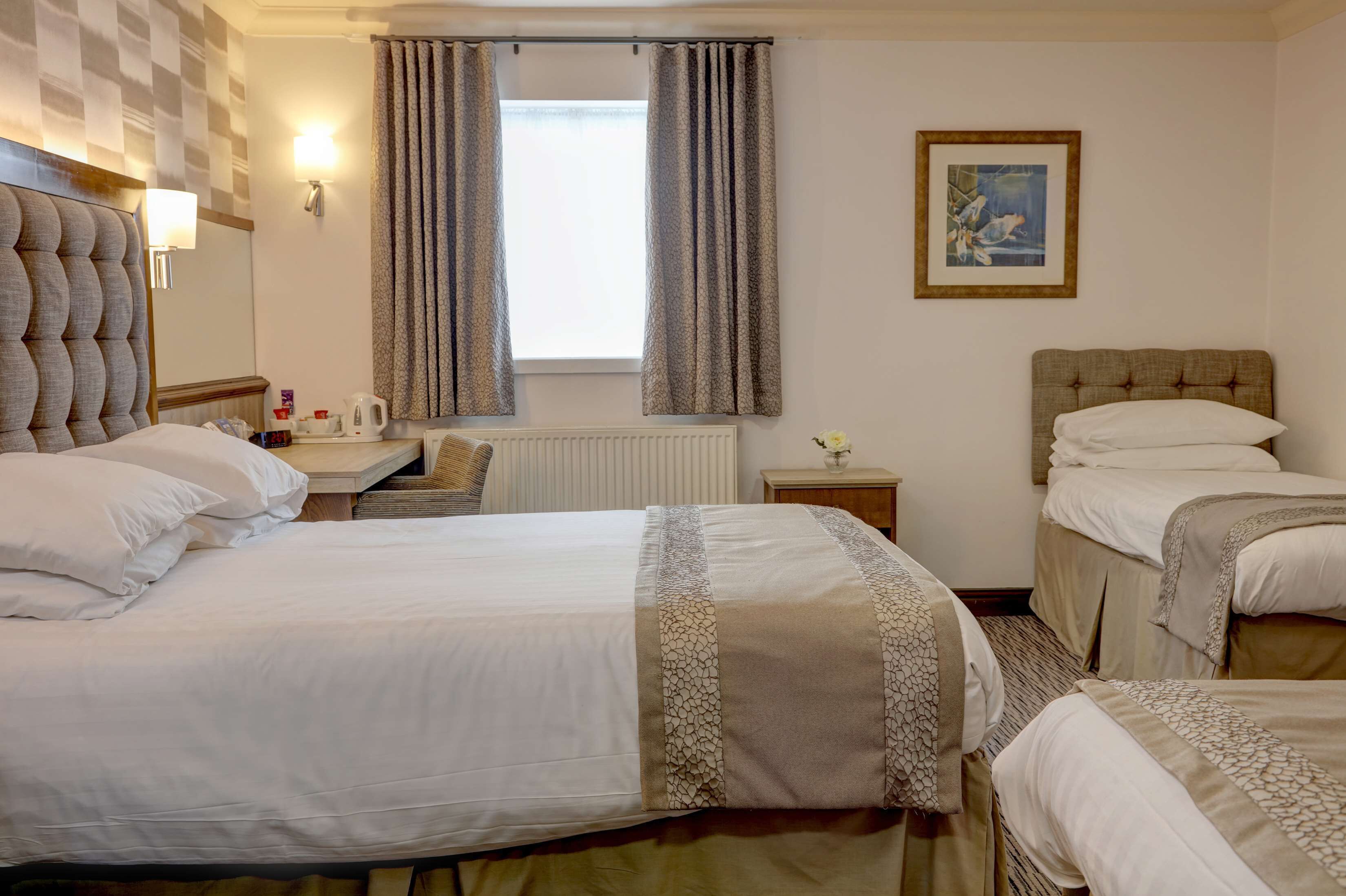 A hotel room with two beds, a desk, a chair, a radiator, and a window with curtains.