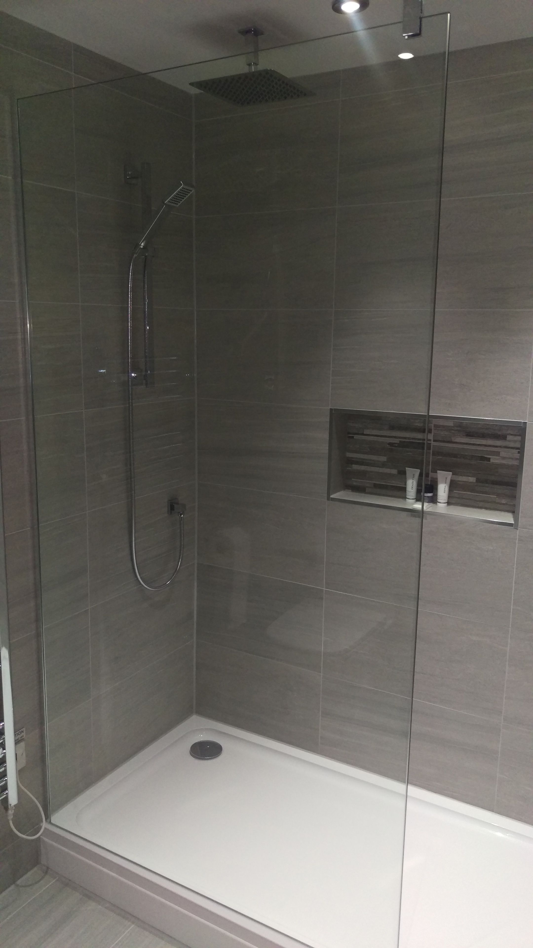 A modern shower enclosure with a glass door, a handheld showerhead, and a built-in shelf with toiletries.